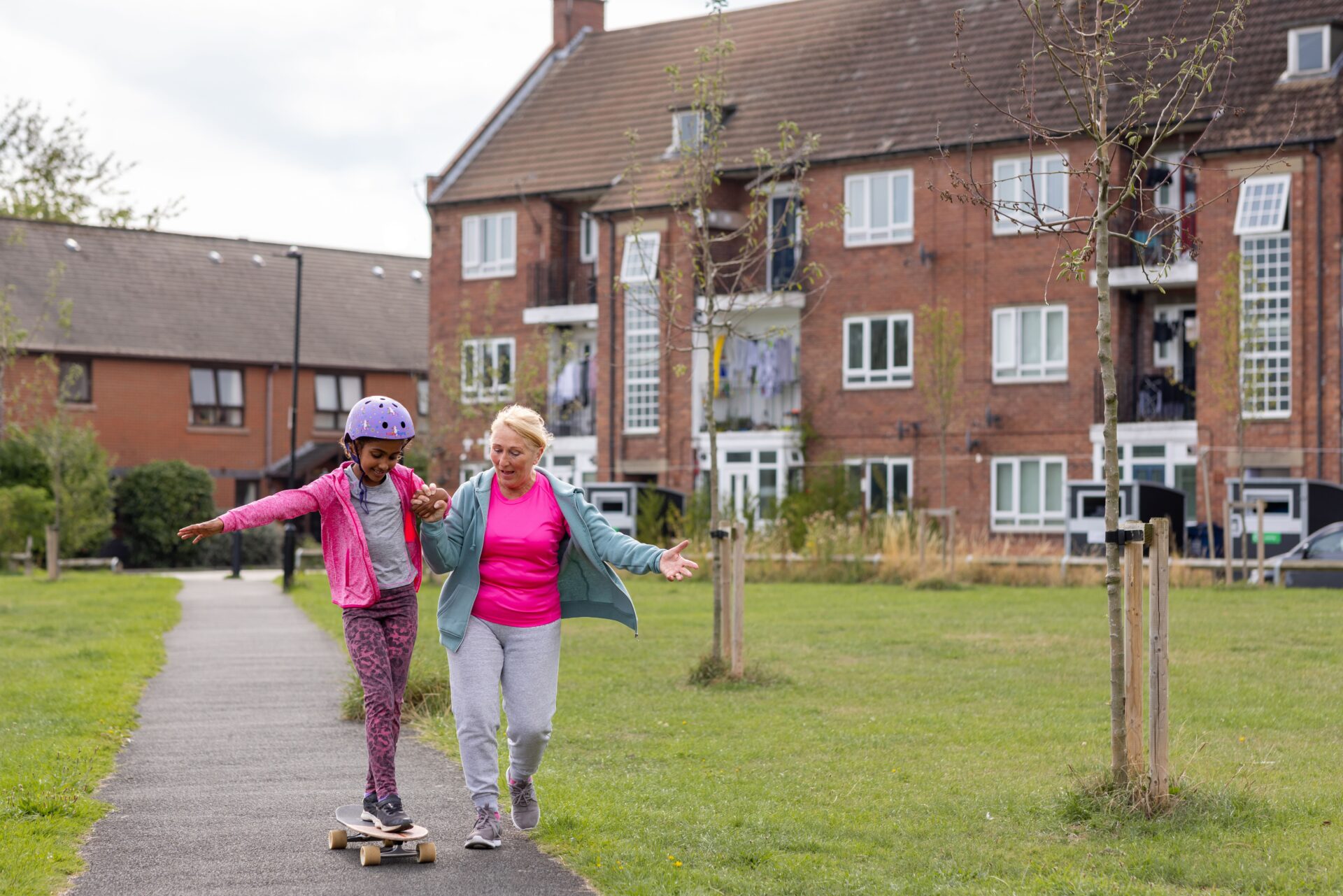 A adult helps a child as they skateboard along a path outside.