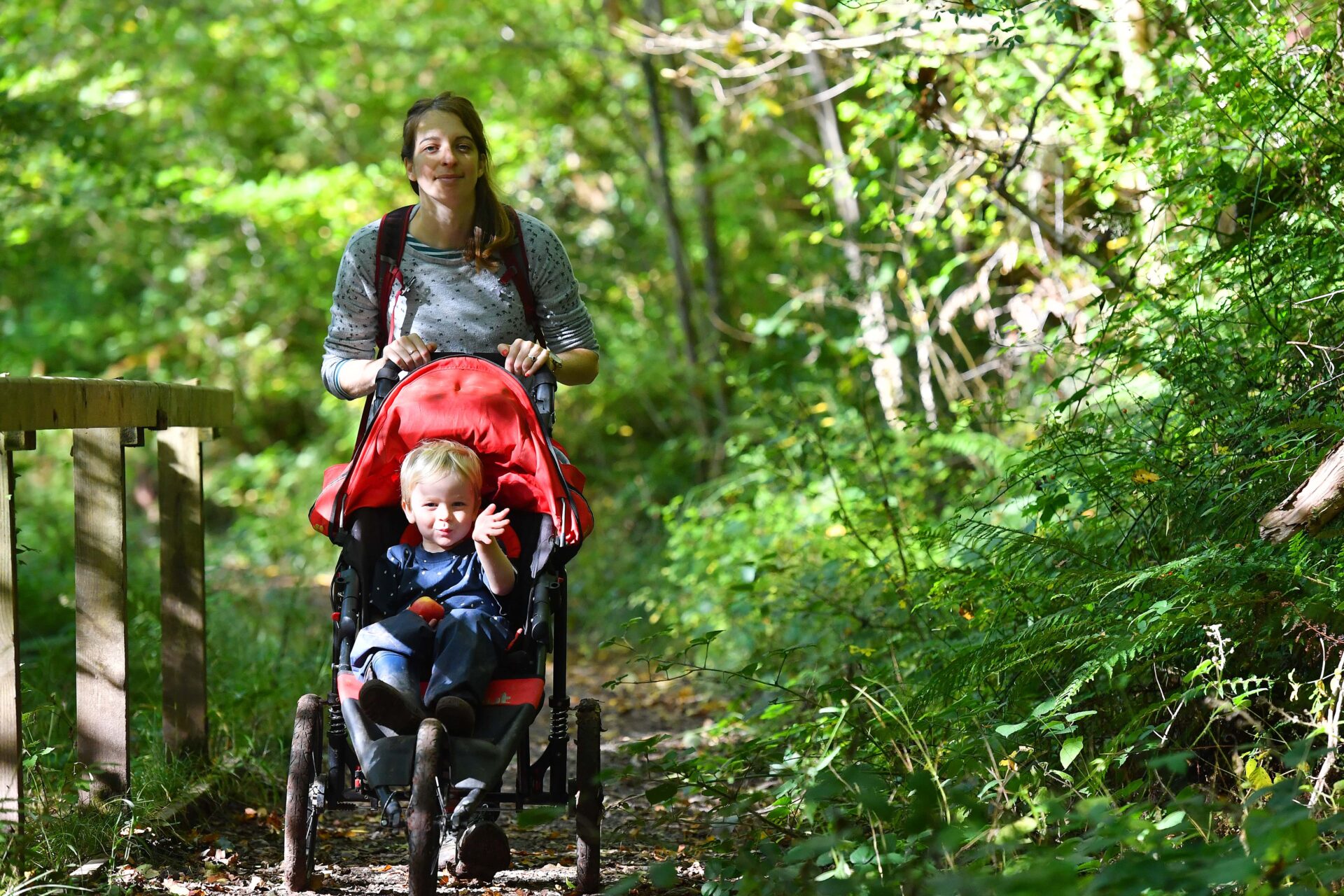 A person pushing a child in a pushchair along a woodland path.