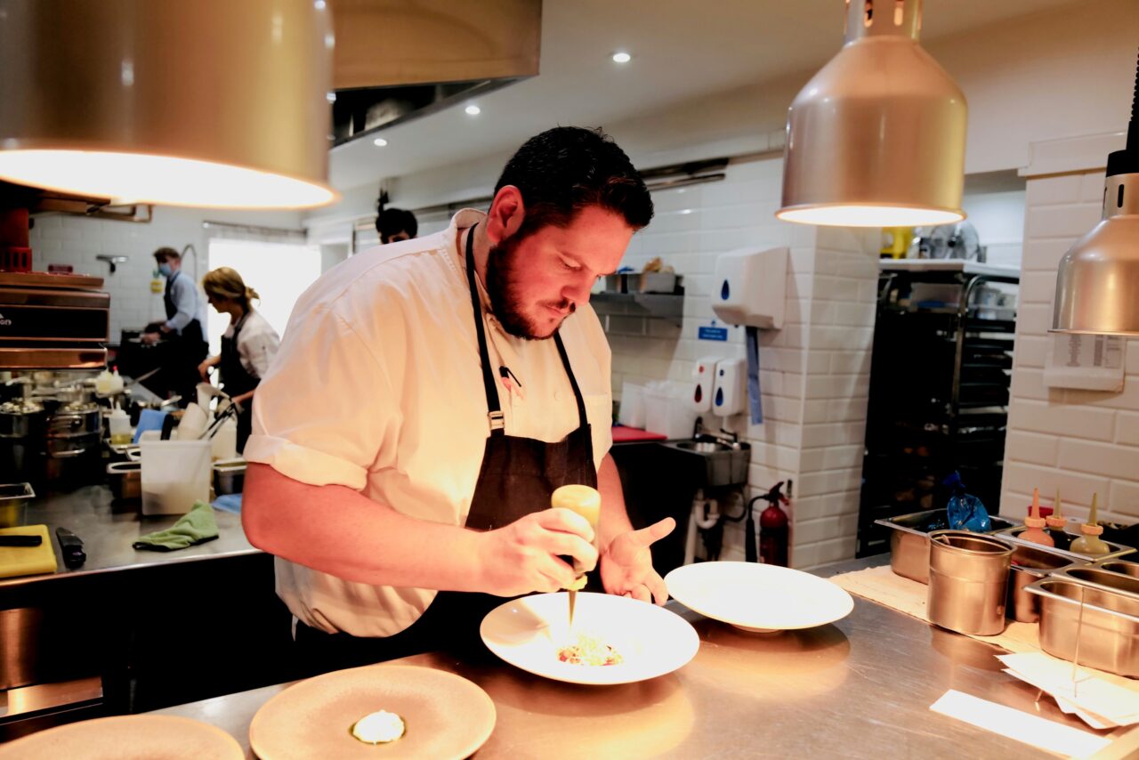 A chef standing over a plate in a kitchen.