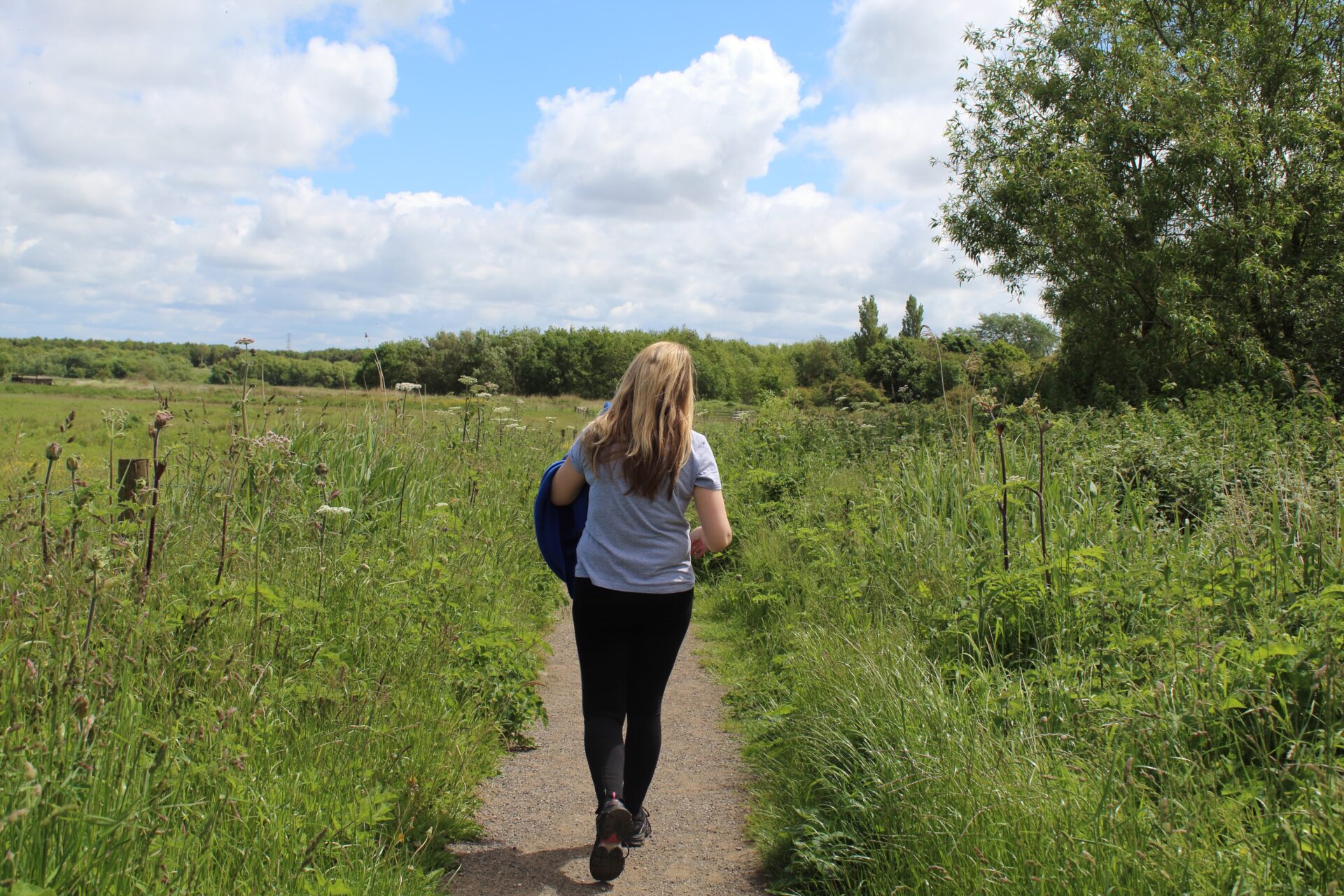 A woman walking down a path surrounded by long grass and trees.