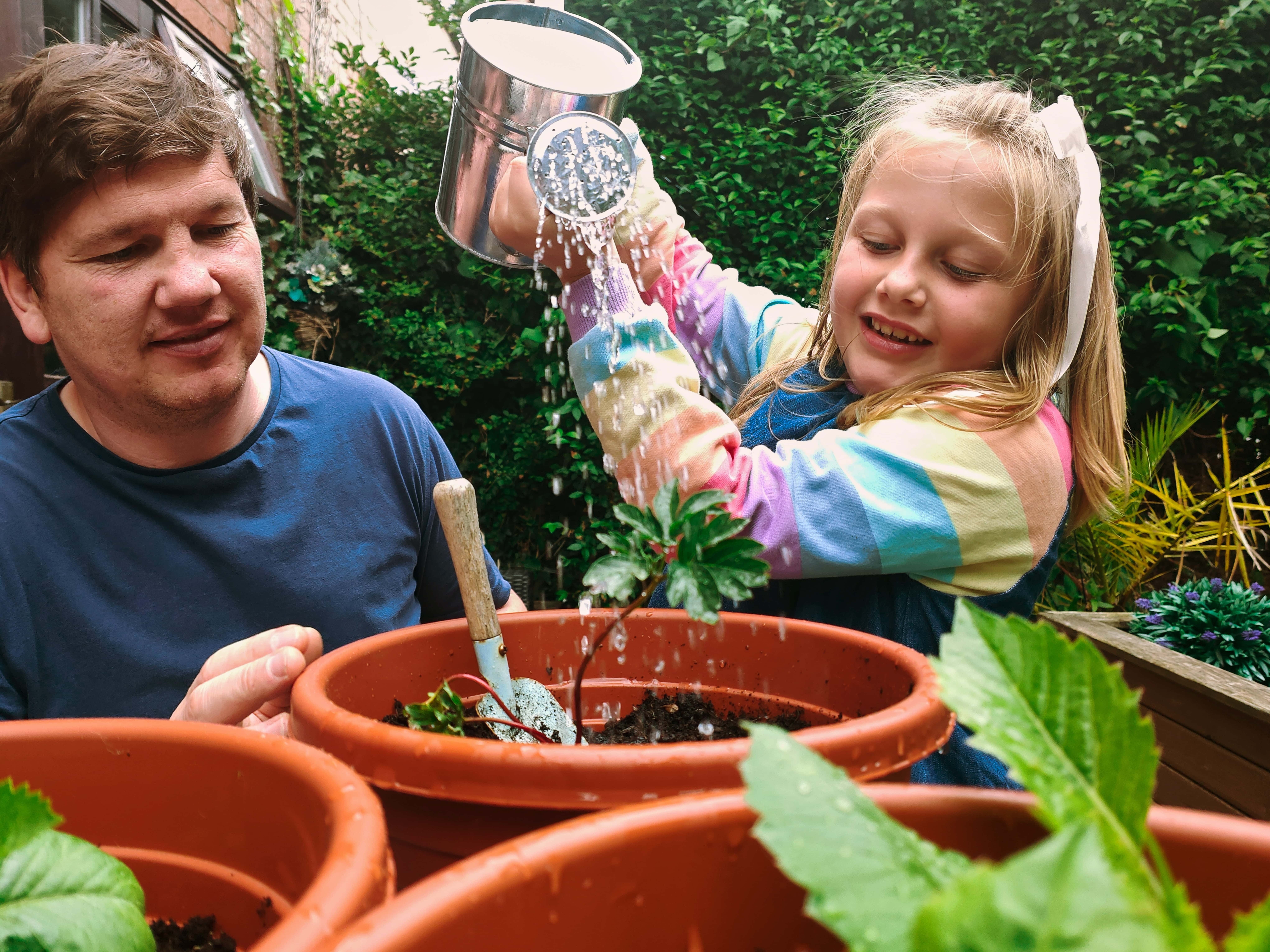 A child gardening with a watering can, as an adult looks on.