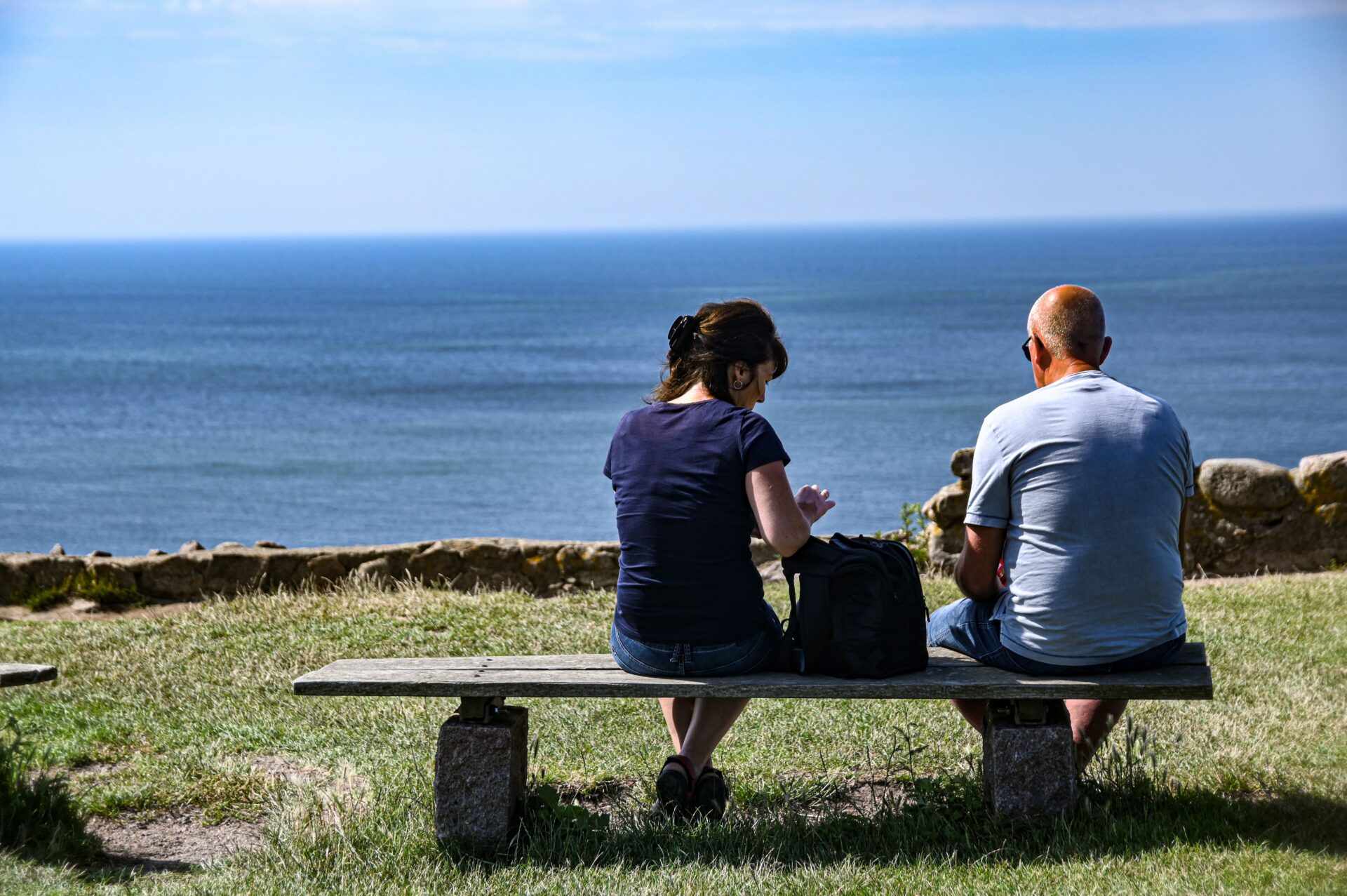 Two people sitting on a bench and looking out at the sea.