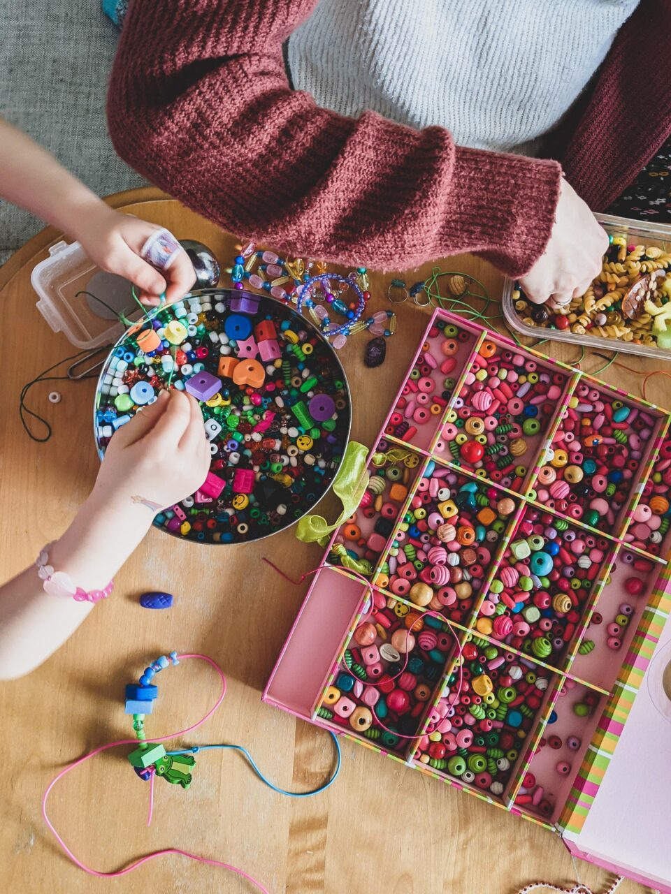 Hands grabbing at an array of beads on a wooden table.