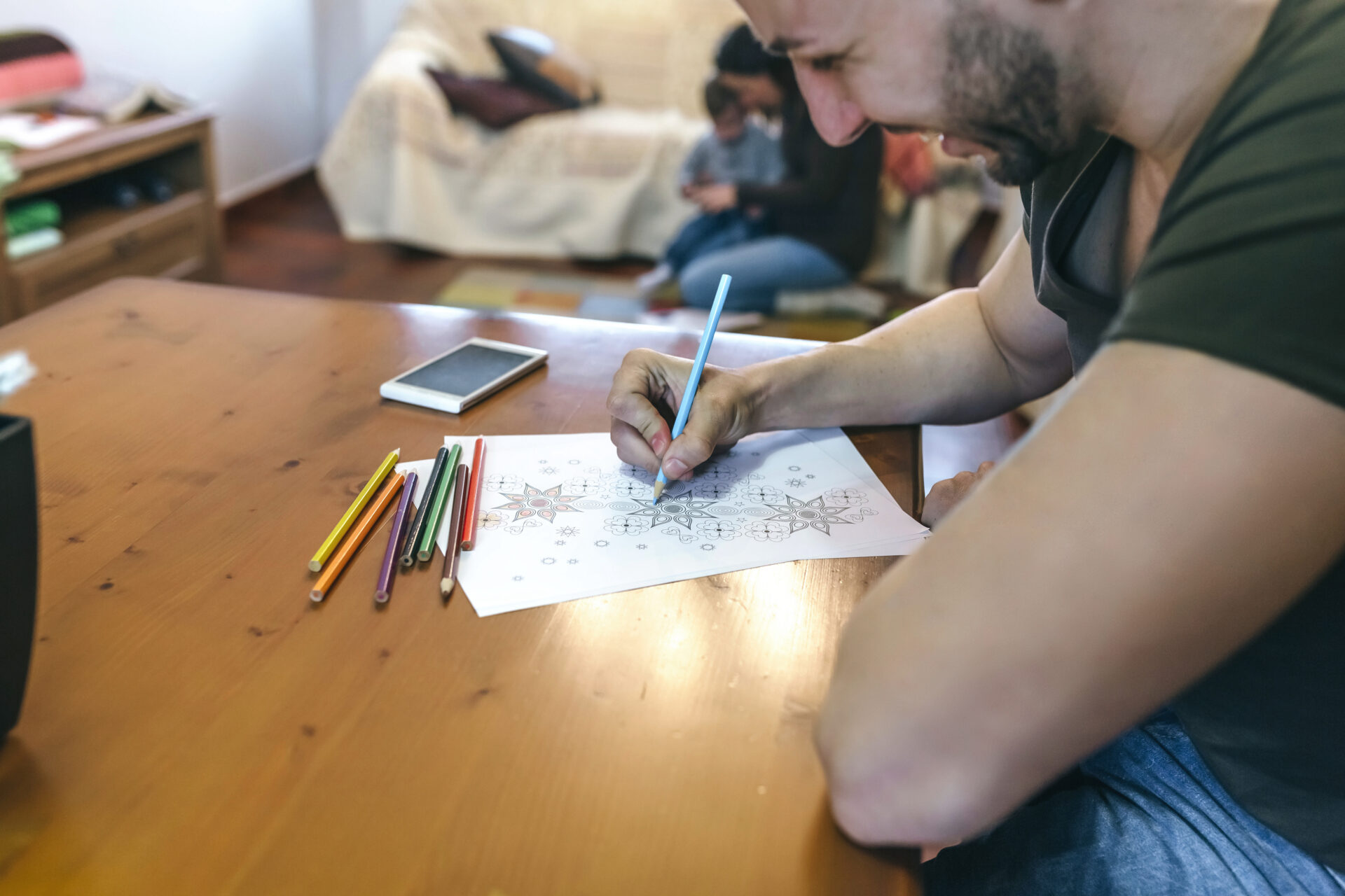 A person sitting at a table, using coloured pencils to colour in on sheets on paper.