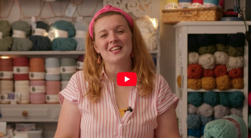A still image of a person with balls of yarn behind them taken from the ‘beginners crochet’ video