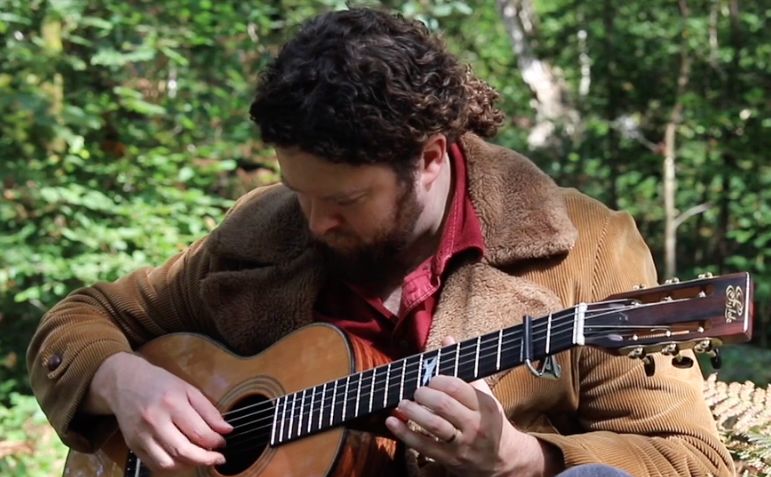 A person sitting outside, playing a guitar.