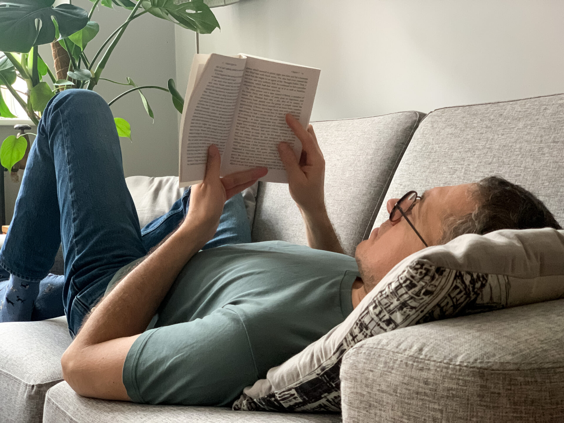 A person lying down on a sofa to read a book