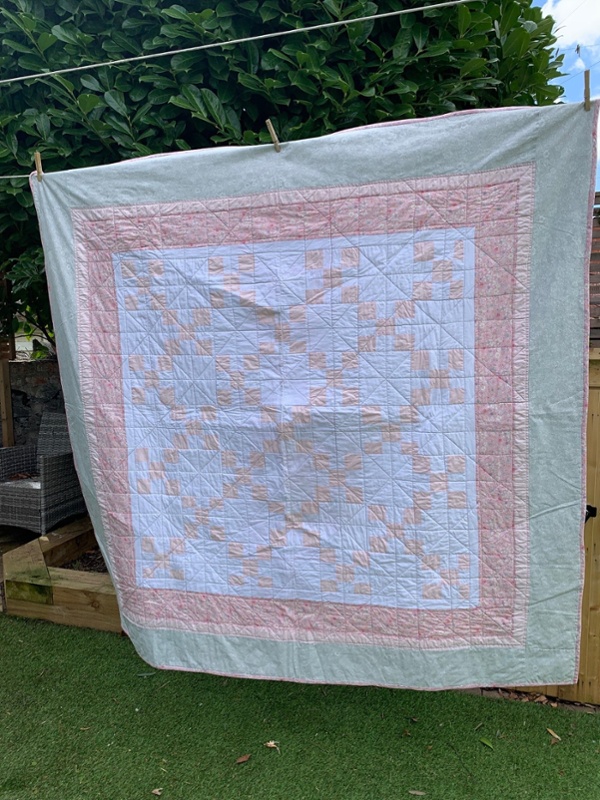 A handmade quilt hanging n a washing line outside