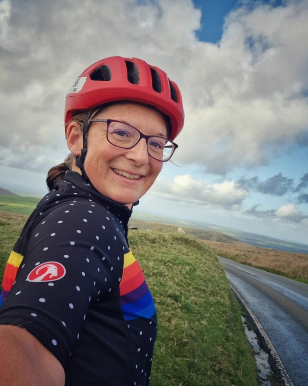 A selfie of a woman wearing a bike helmet on the side of a rural road