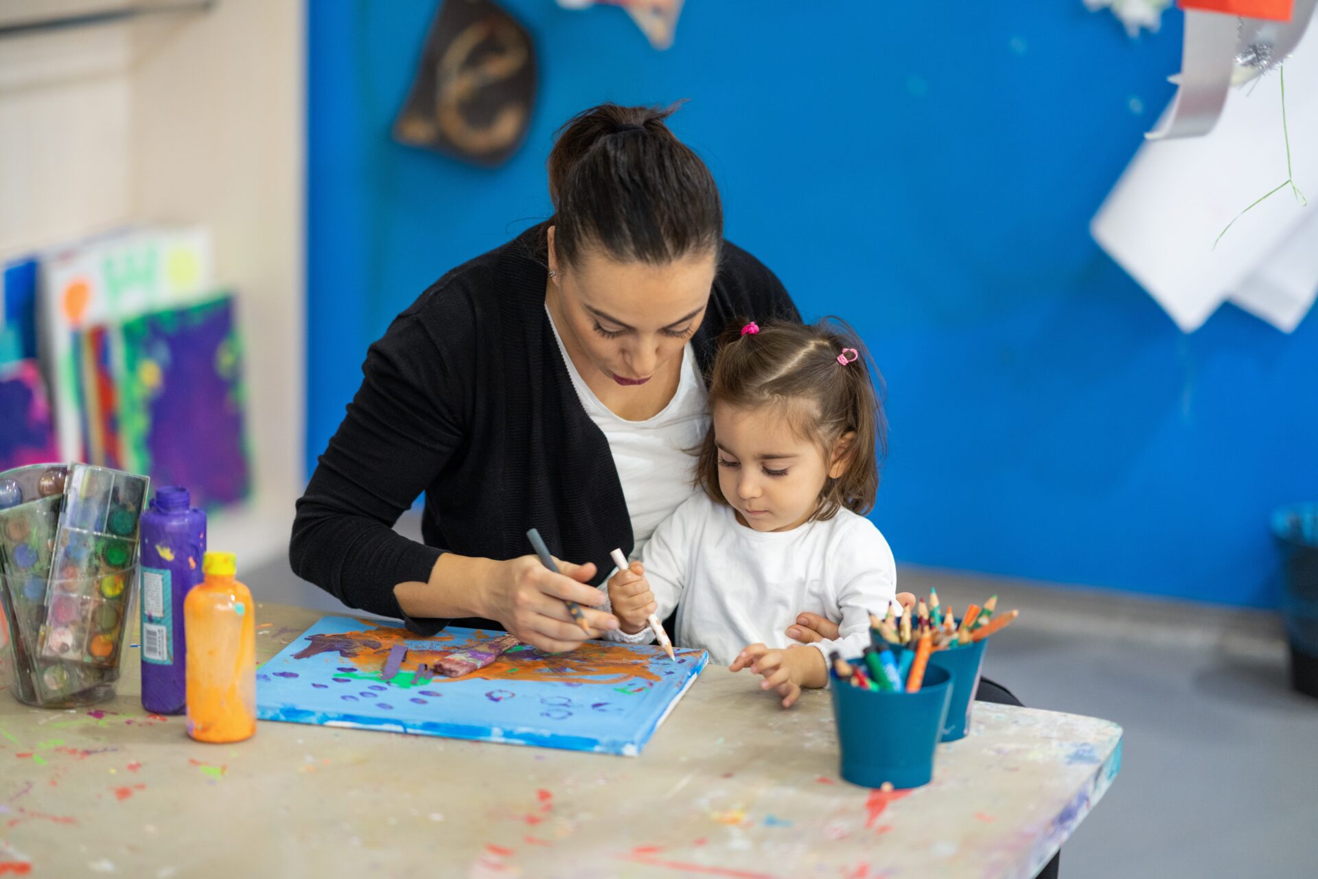 A mother and her daughter sitting at a table making a picture together.