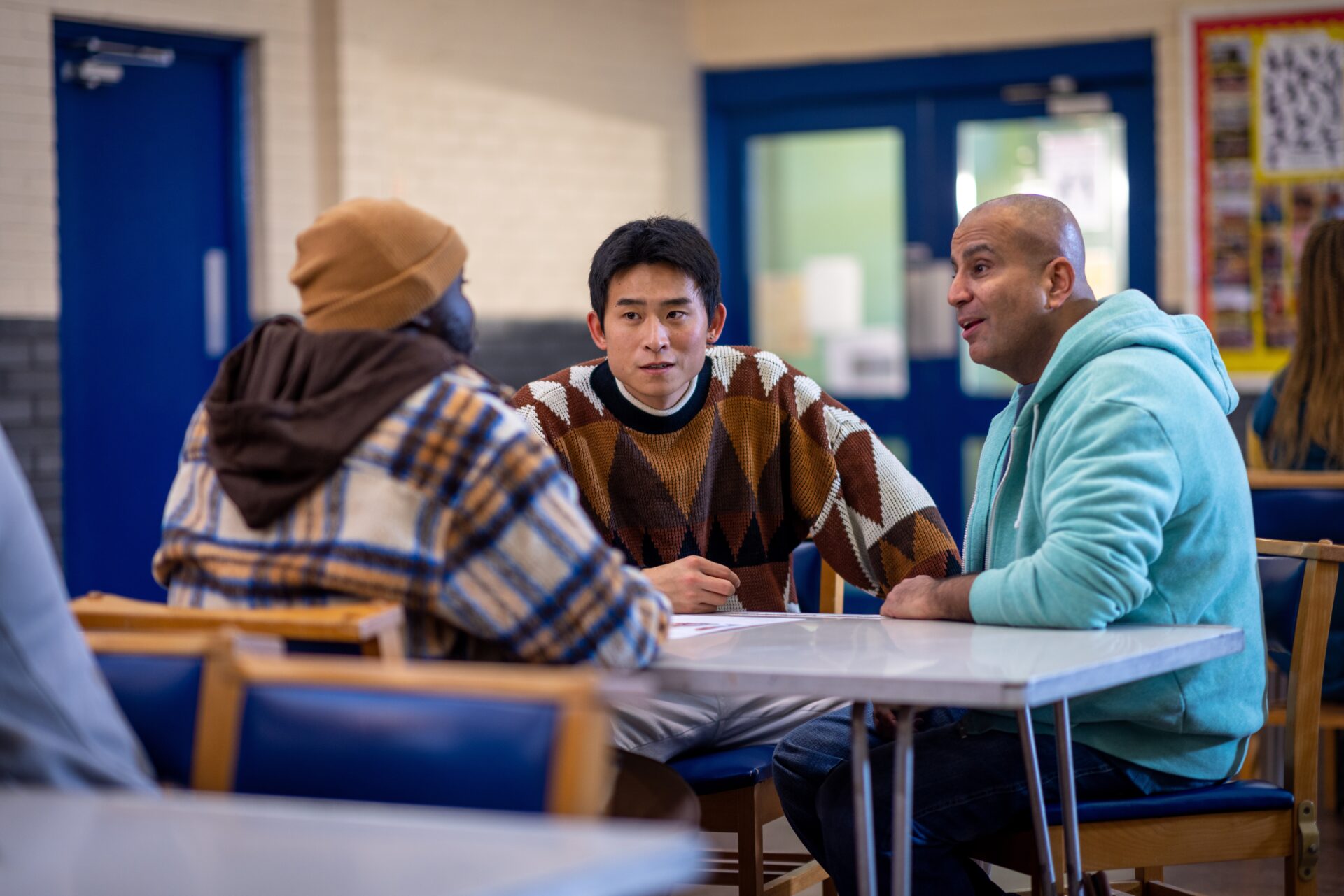 A group of people talking to each other while sat at a table