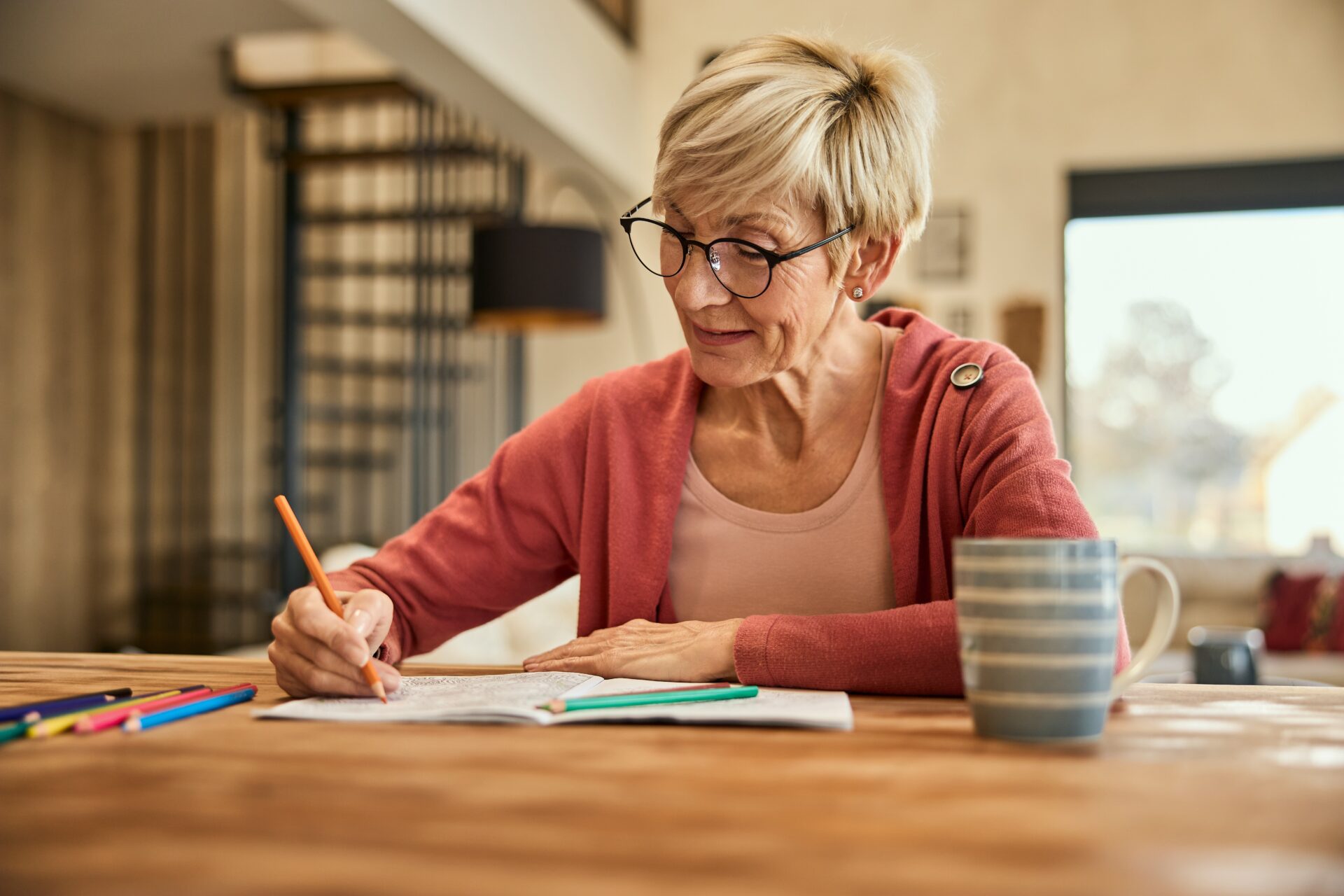 A woman sat at a table using coloured pencils in a colouring in book