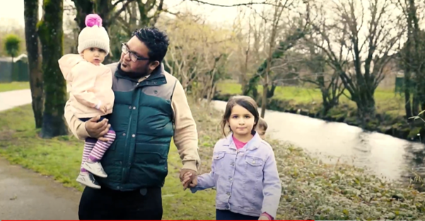 A father and two children walking along a path next to a river.