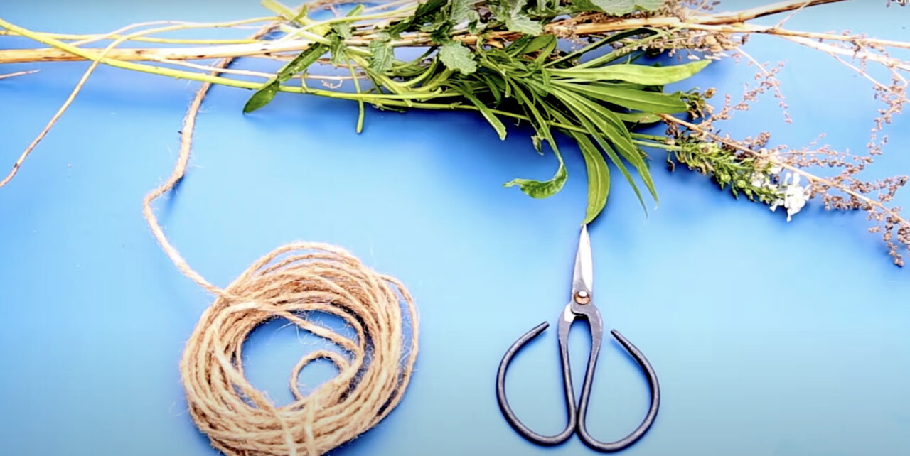 A scissors, ball of string and a bunch of flowers on a blue background.