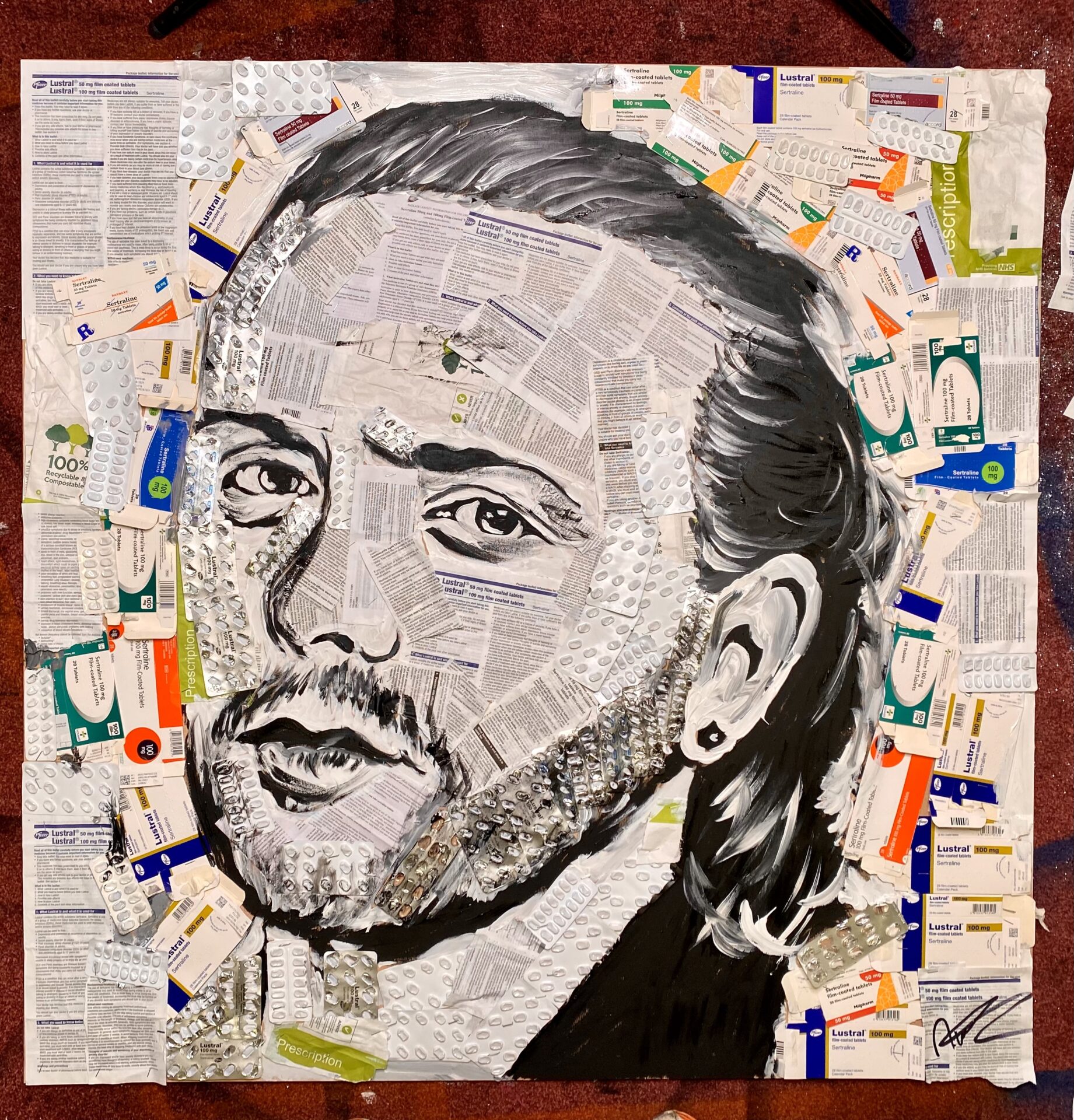 A portrait of a person with a beard and swept back dark hair. The portrait is made from black marker and old prescription packaging.