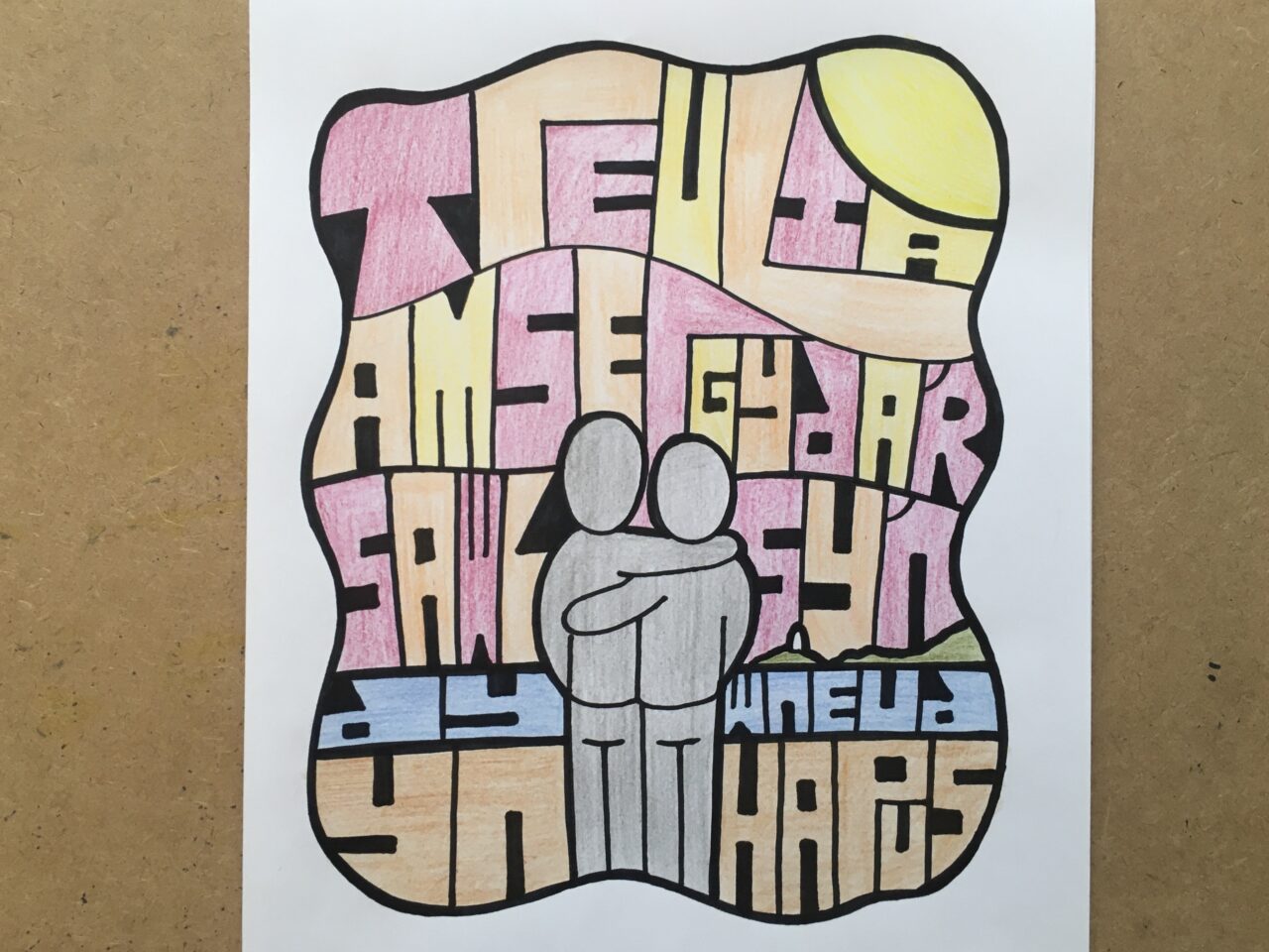 A drawing pinned to a corkboard. On the drawing are these words: 'Treulia amser gyda’r sawl sy’n dy wneud yn hapus'. Two grey people icons are hugging in the middle.