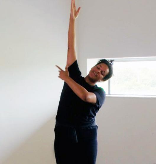 A person standing in a brightly lit white room with their right arm extended toward the ski and their right arm extending across their body and pointing to the right. Their head is leaning off to the left.